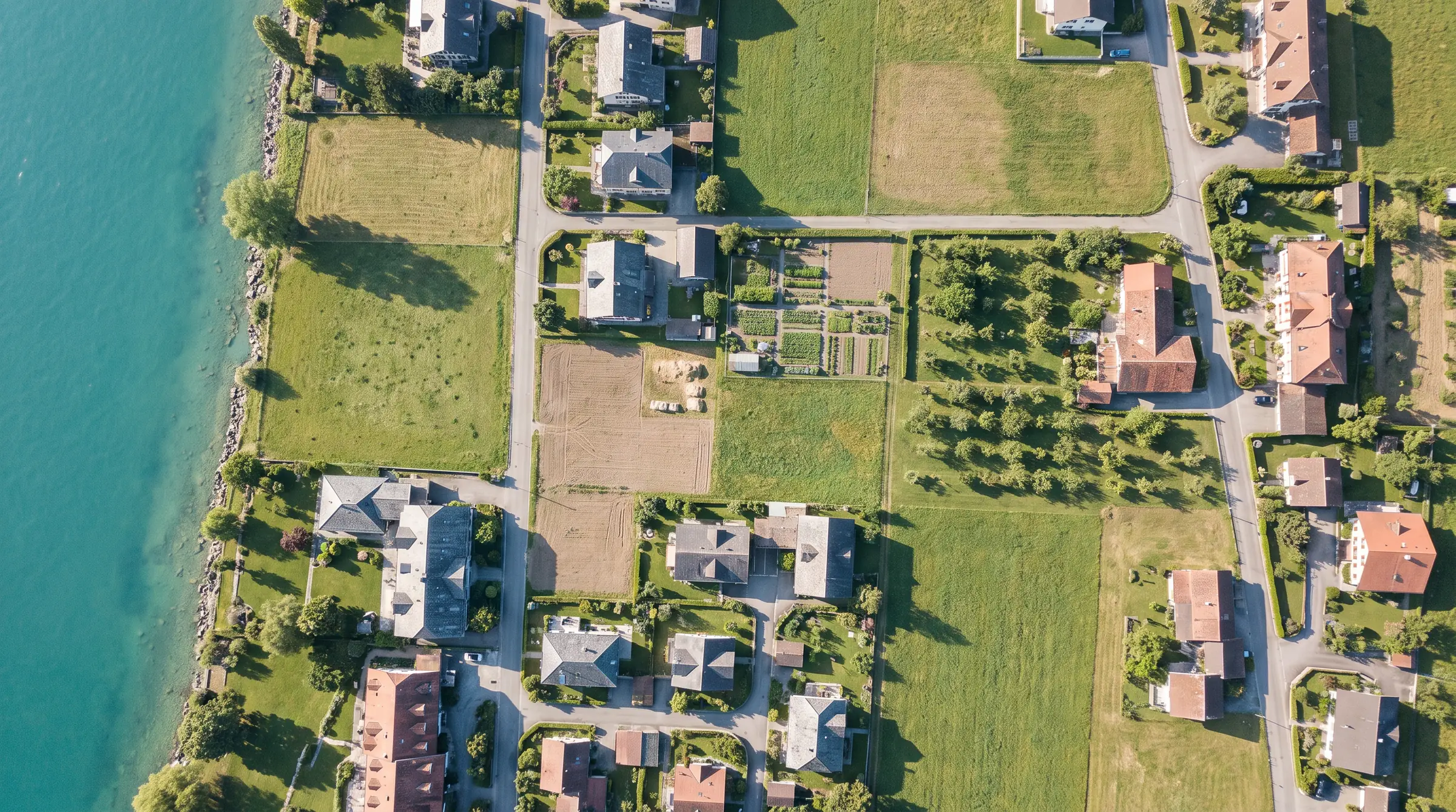 Luftaufnahme senkrecht von oben auf ein Dorf am Seeufer mit Wiesen, Grundstücken und Gärten