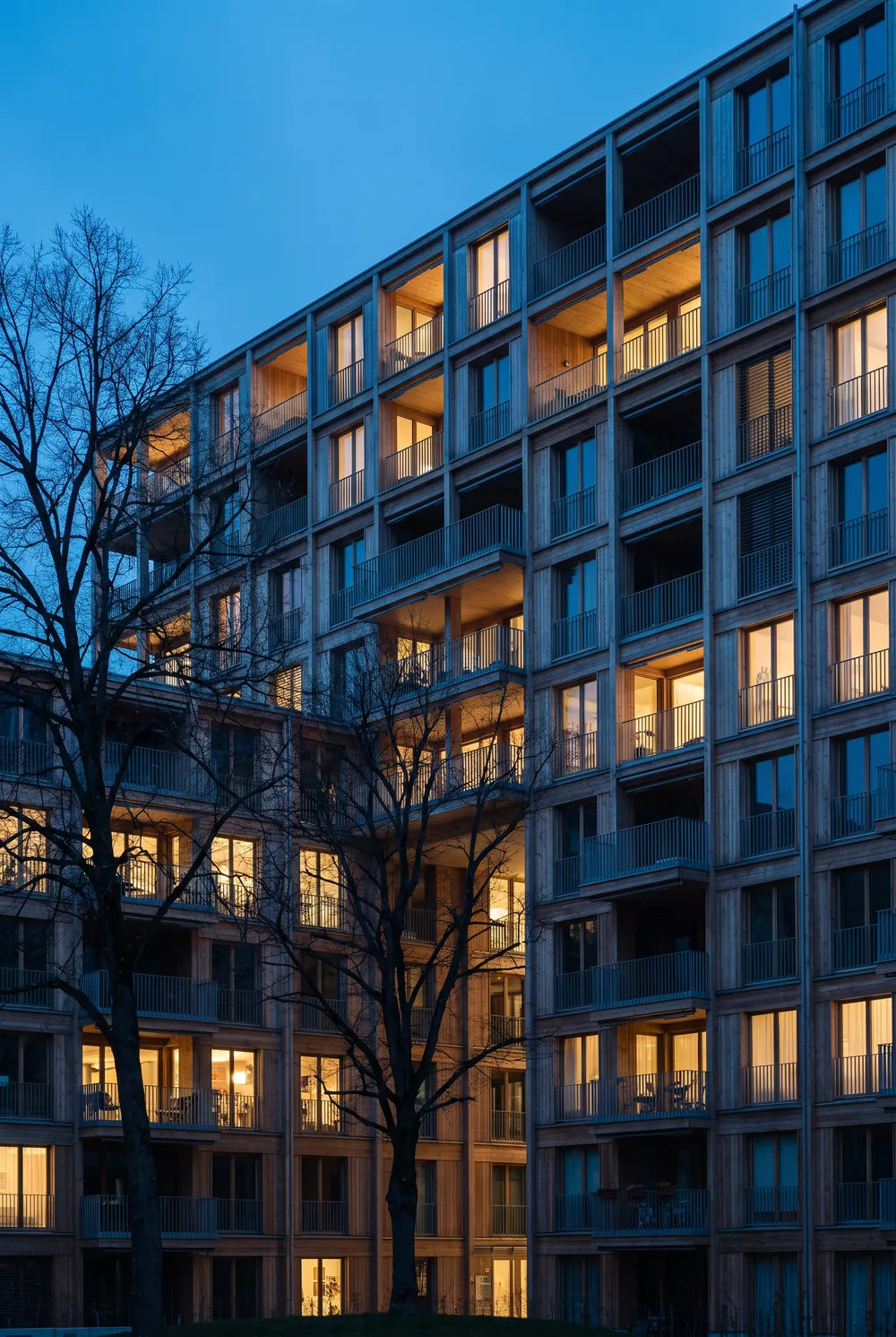 Grosse moderne Wohnüberbauung mit Balkonen und Bäumen im Innenhof in der Abenddämmerung